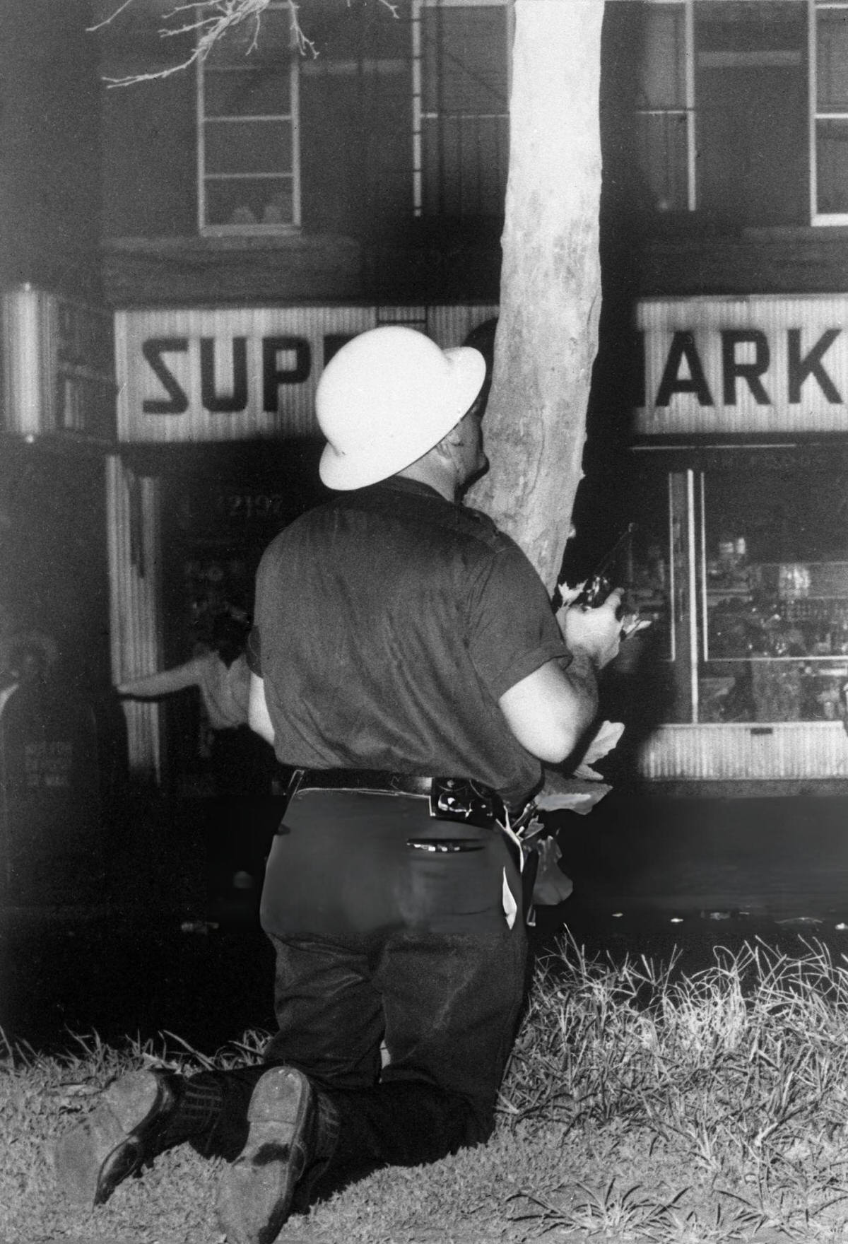 Police Officer With Drawn Gun Using A Tree For Cover During The Harlem Riots, 1964.