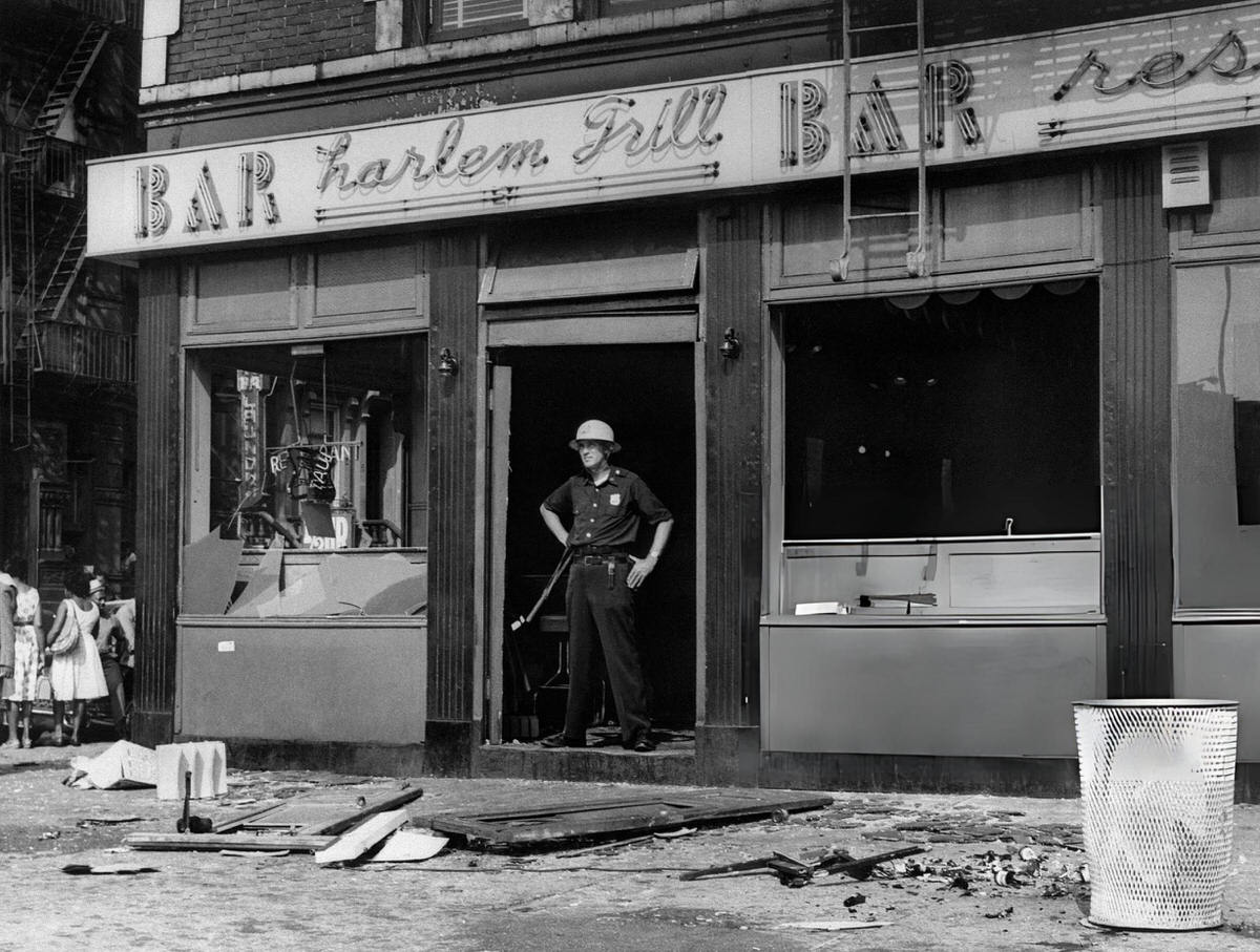 Police Officer Standing In Front Of A Destroyed Bar On 126Th Street, Harlem, 1964.