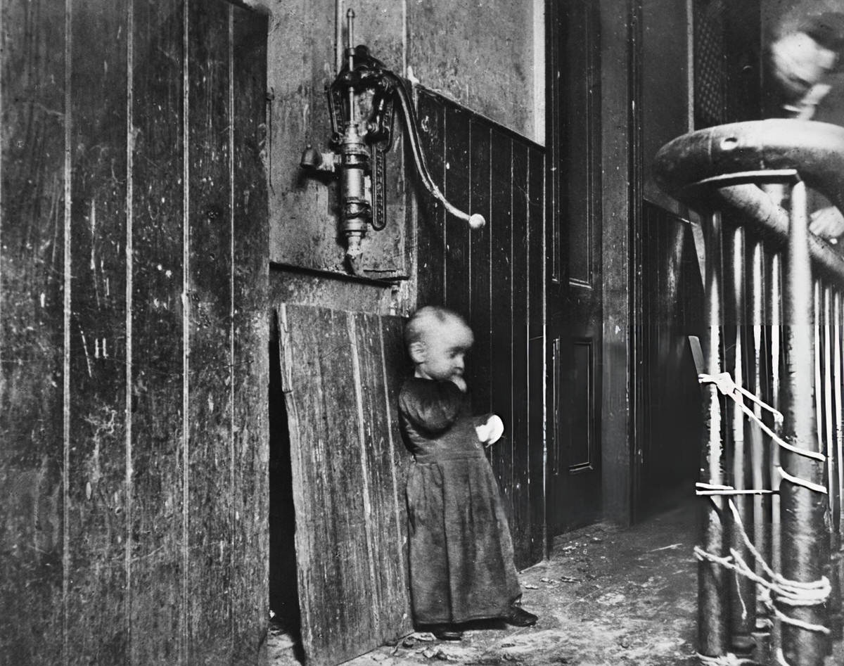 Boy In The Hallway Of A Tenement Building With A Water Pump, New York, 1890.
