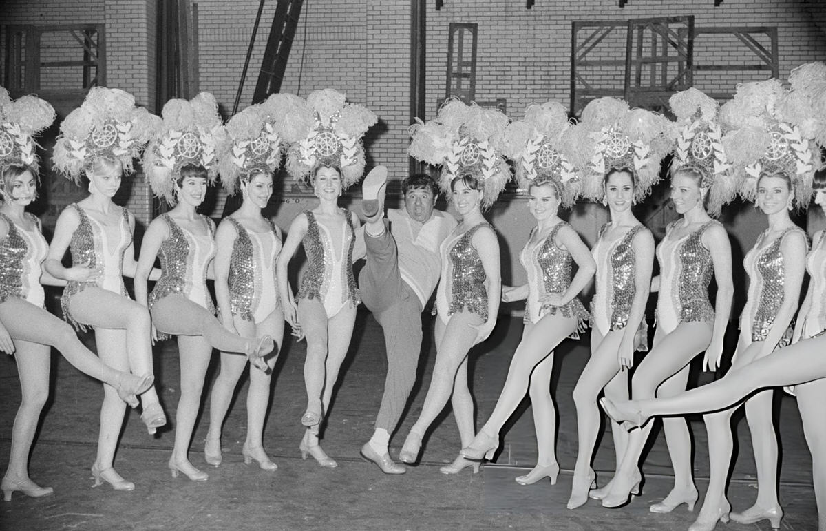 Comedian Buddy Hackett Posing With The Rockettes Backstage At Radio City Music Hall, New York, 1969.