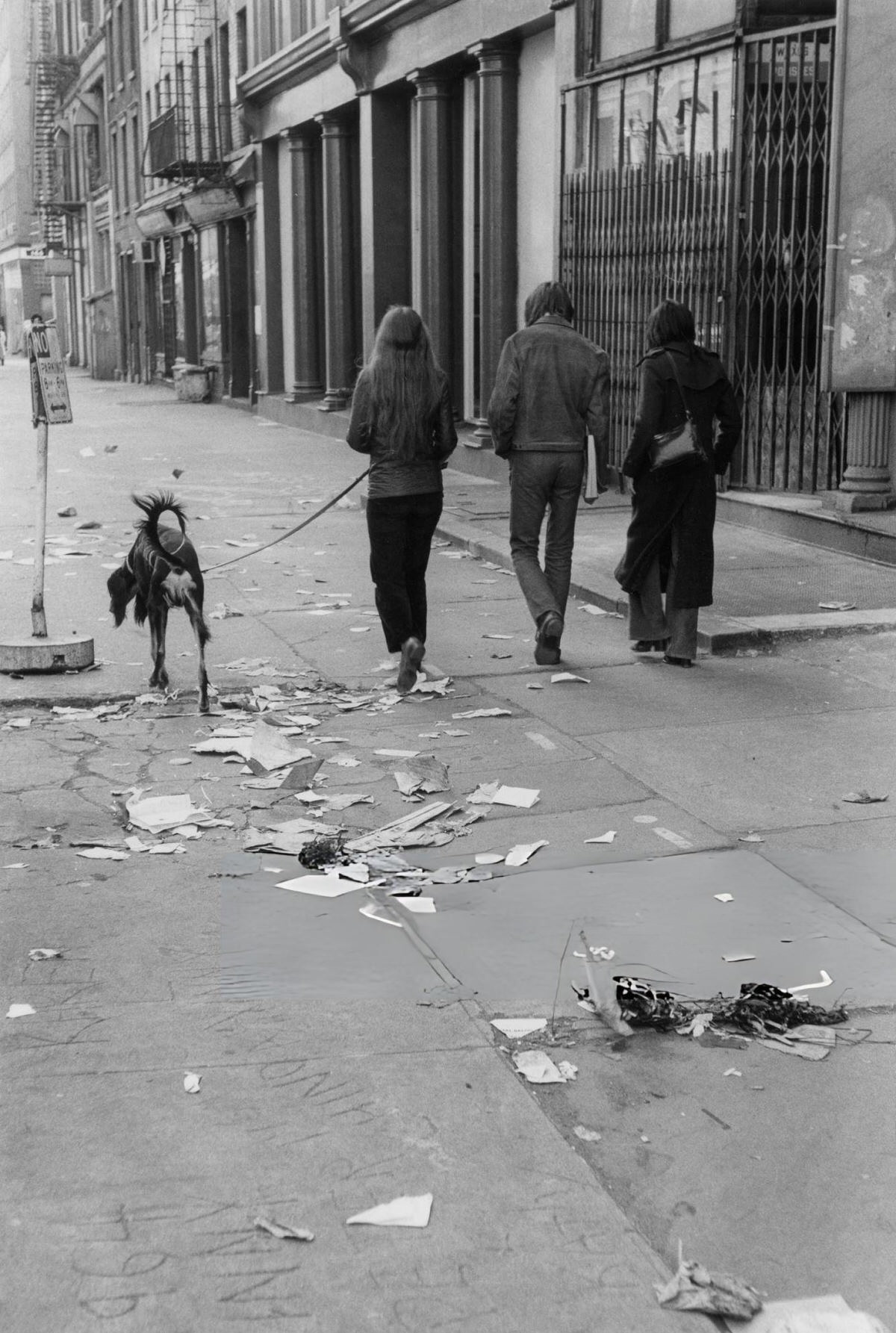 People Walking A Dog Along A Trash-Strewn Street In Soho, 1972.