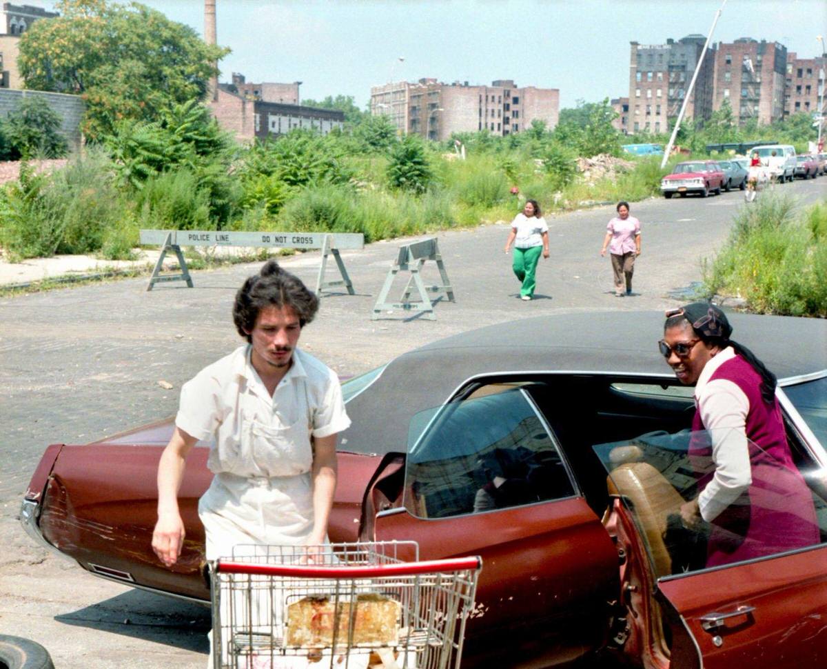 Shop Worker Helping A Woman Load Groceries Into A Car On A Desolate Street, South Bronx, 1980.