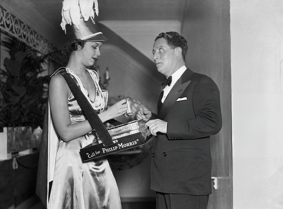 Comedian Bert Wheeler Buying Cigarettes From A Vendor At The Cotton Club, New York, 1936.