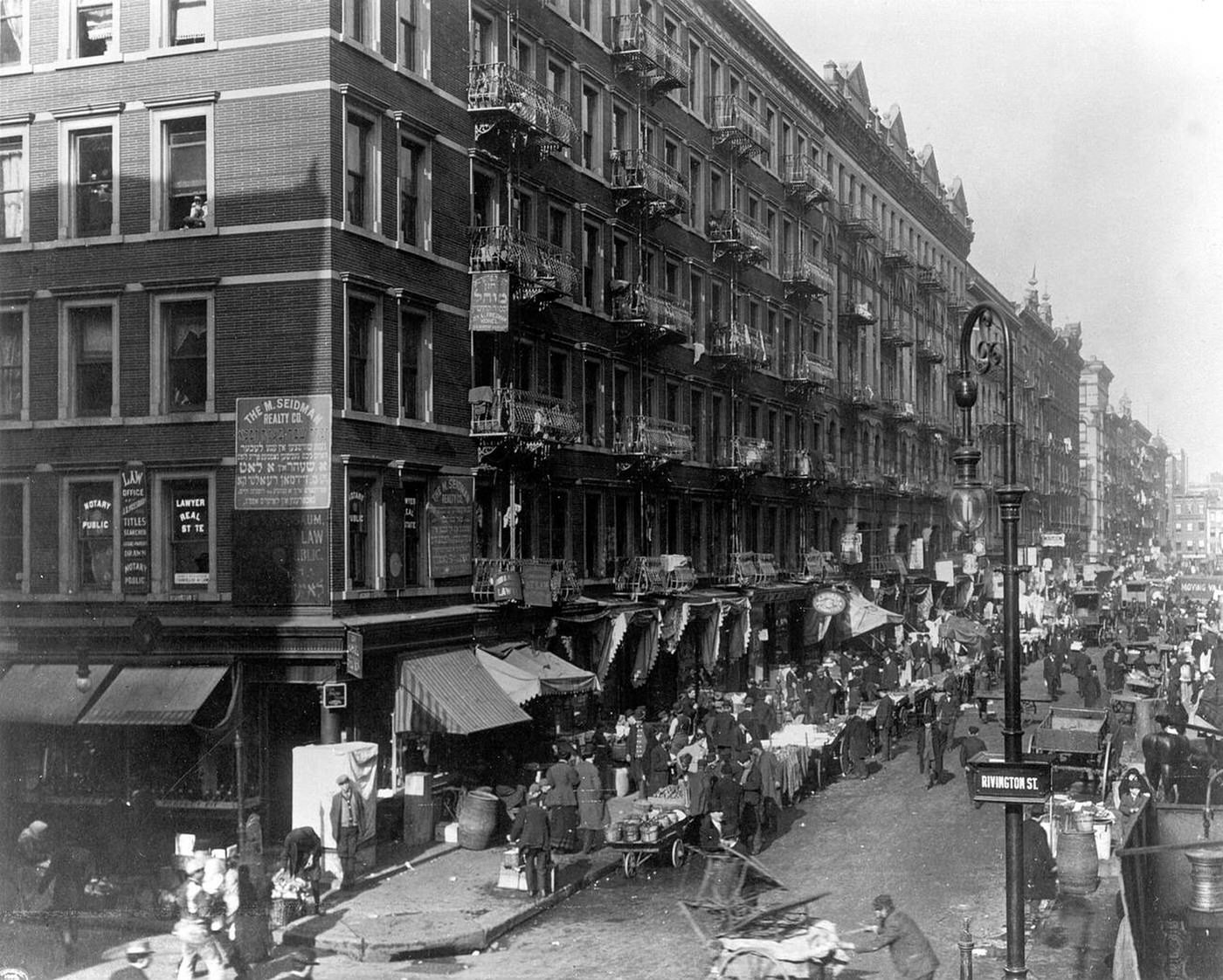 Electric Street Lamp On A Busy City Street Lined With Vendors And Carts, New York City, 1909
