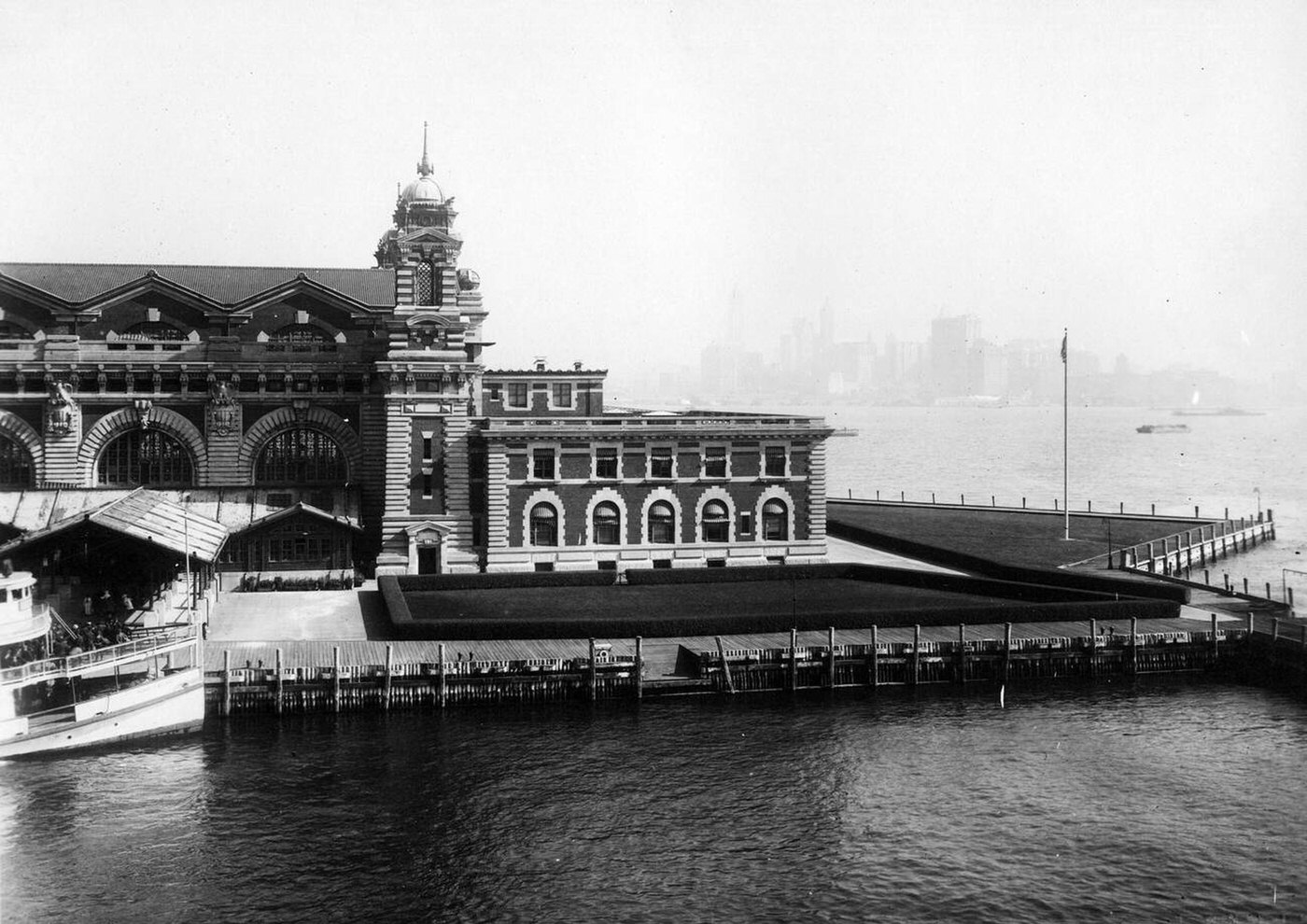 Front Facade Of The Ellis Island Immigration Inspection Station With People Exiting A Boat, 1907