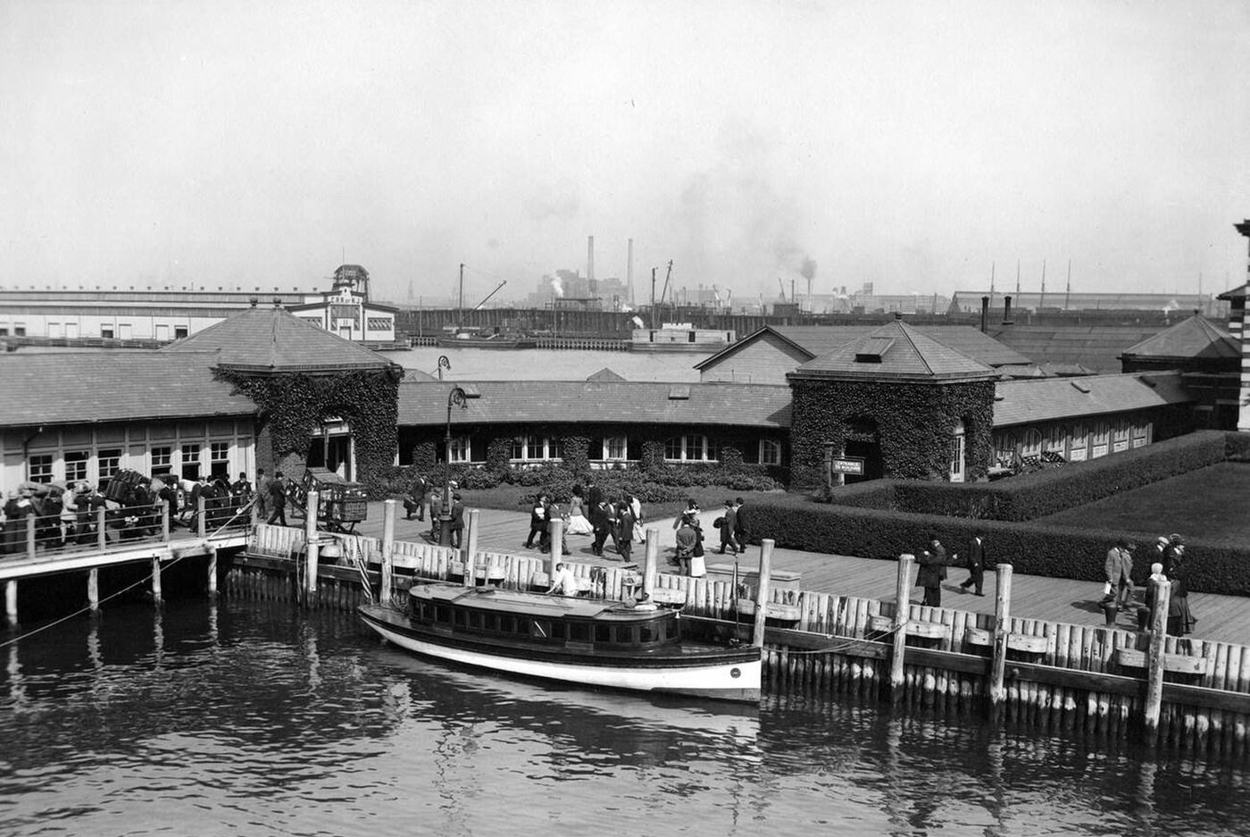 Buildings Near The Ellis Island Pier With Immigrants And Luggage On The Boardwalk, 1907