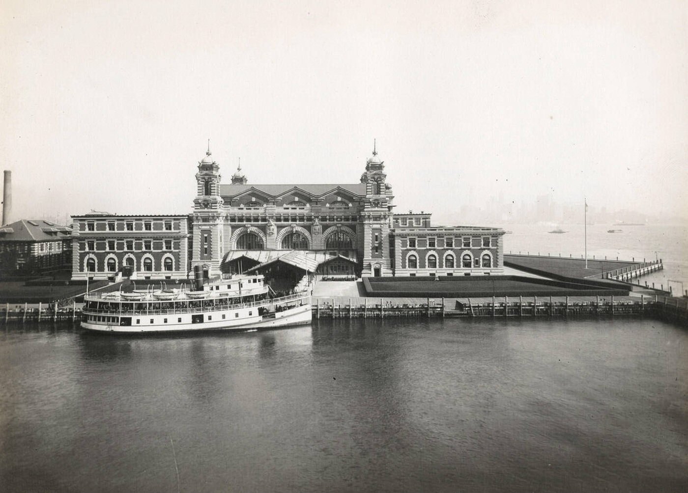 Front Facade Of The Ellis Island Immigration Station With A Boat Docked In Front, 1902